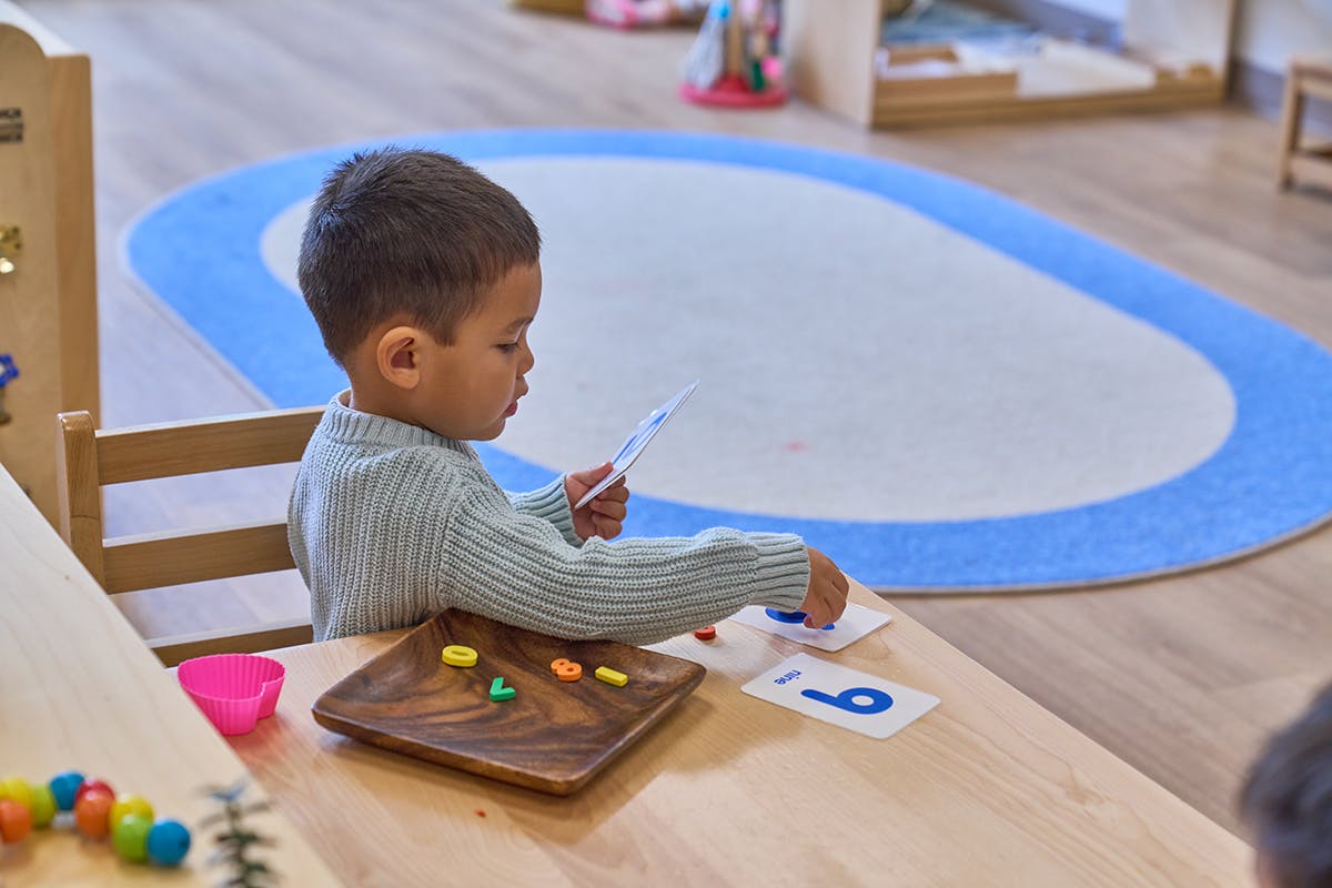 Child sitting at a table, holding a card and playing with small objects