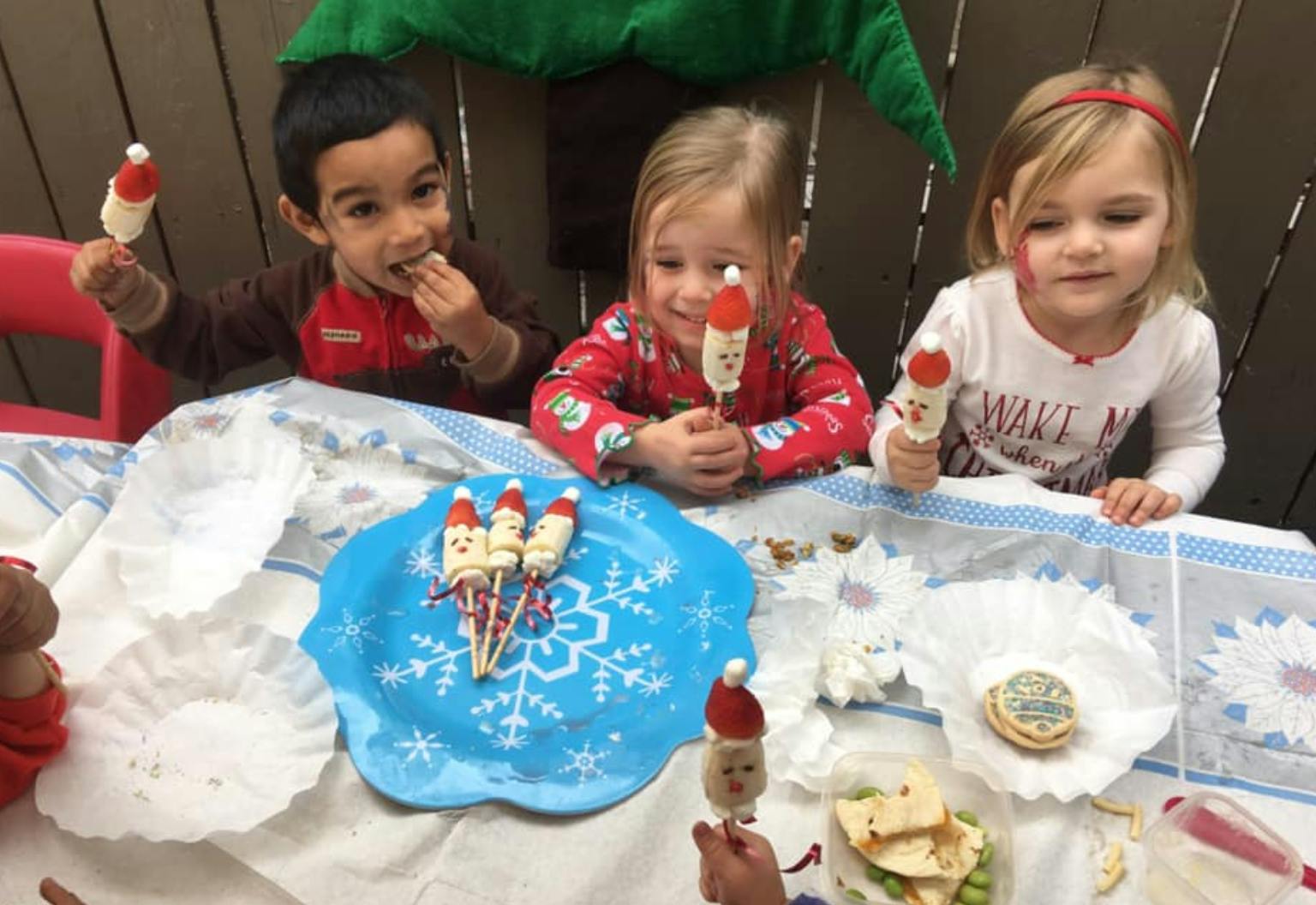 Three children at a table with food, holding treats on sticks