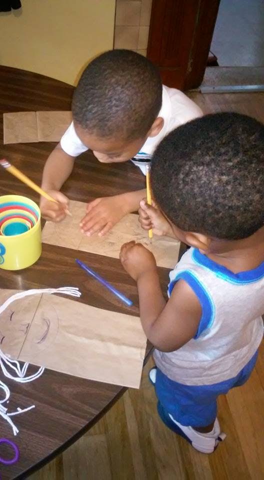 Two children drawing on paper bags with pencils