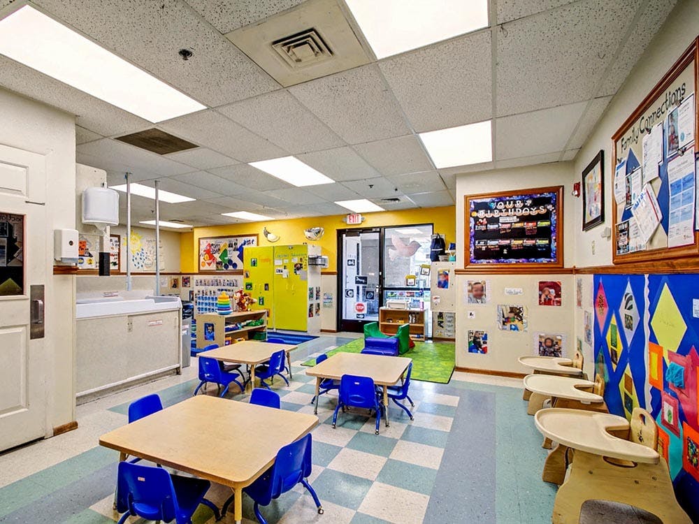 Classroom with small tables and chairs, baby high chairs, and decorated walls