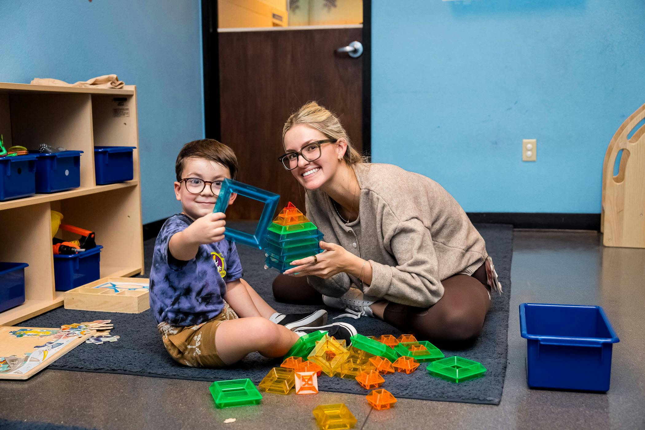 A person and a child sitting on a rug playing with colorful magnetic blocks
