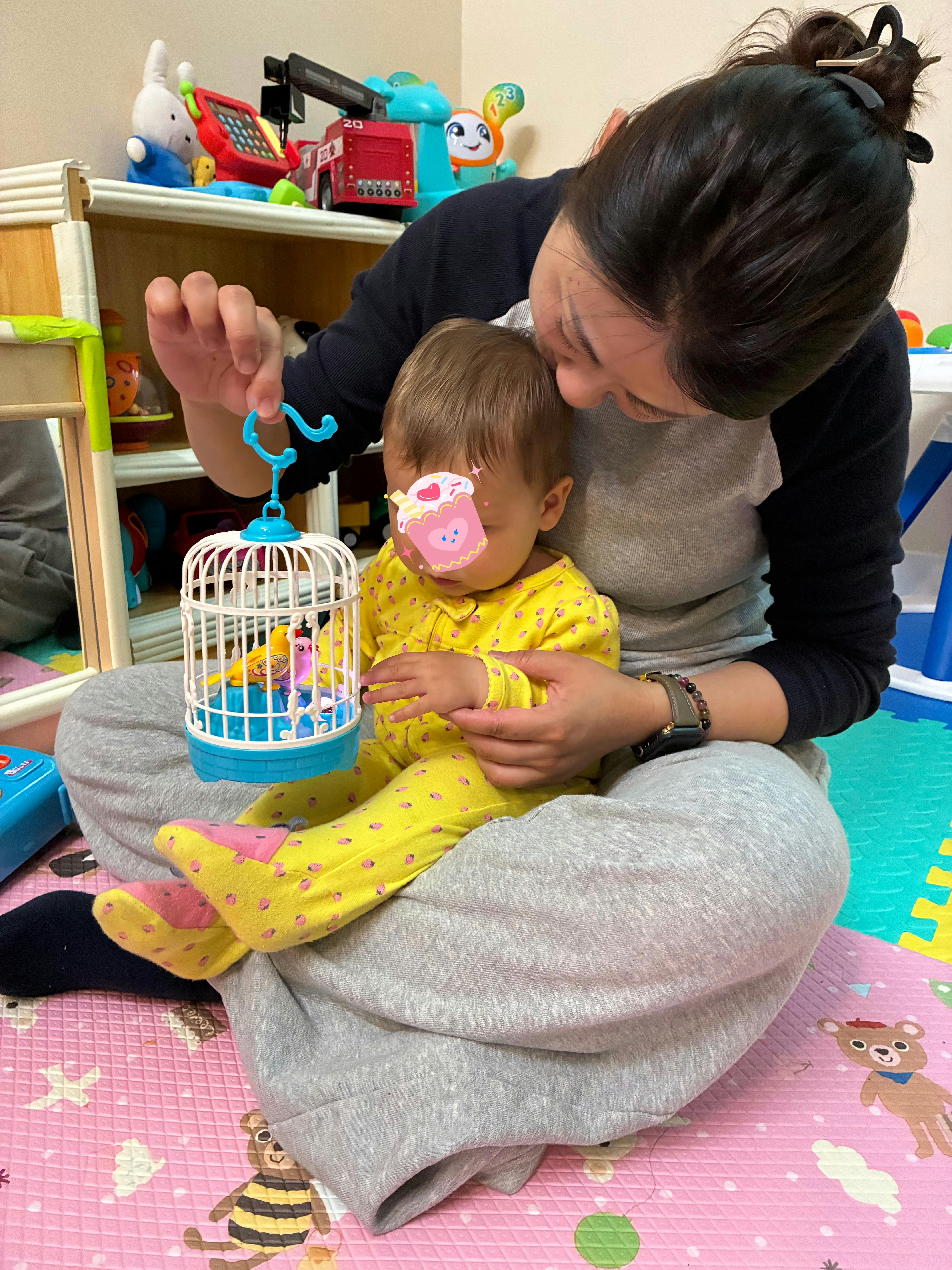 Adult holding a toy birdcage for a child sitting on their lap