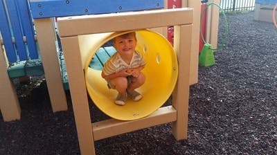 Child crouching inside a yellow tunnel on a playground