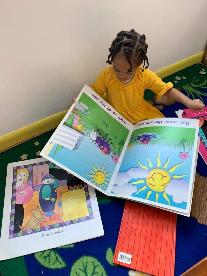 Child in a yellow dress reading a picture book with a sun illustration