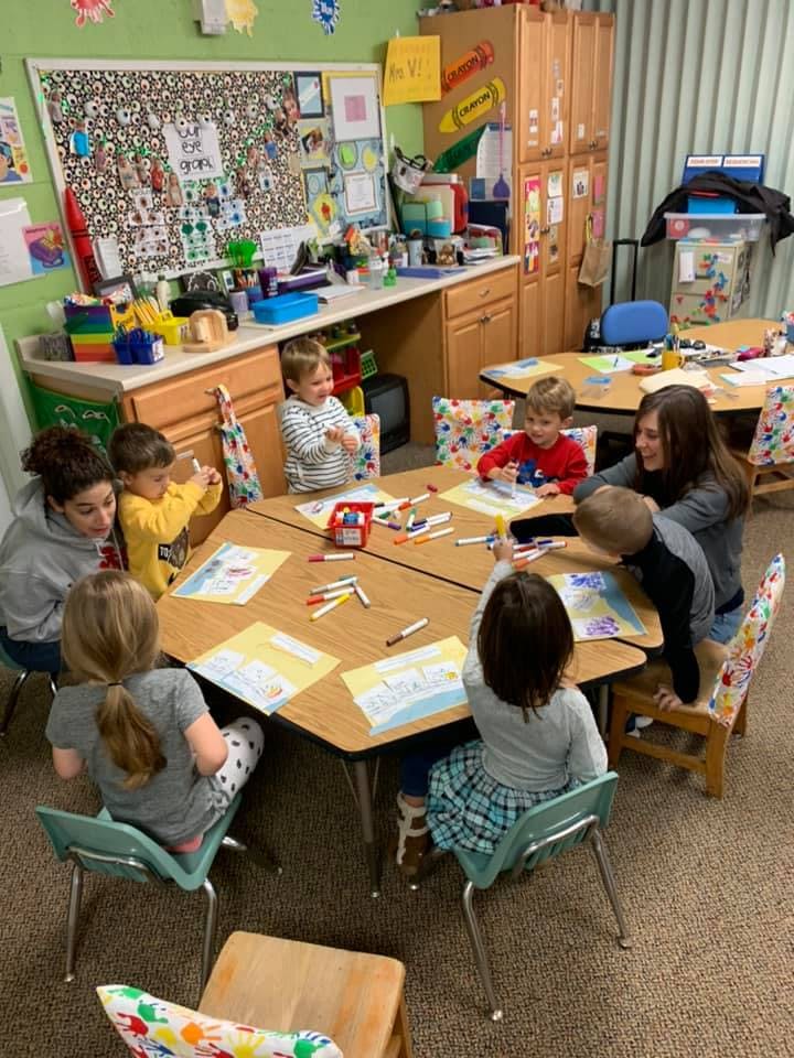 Adults and children drawing at tables in a classroom