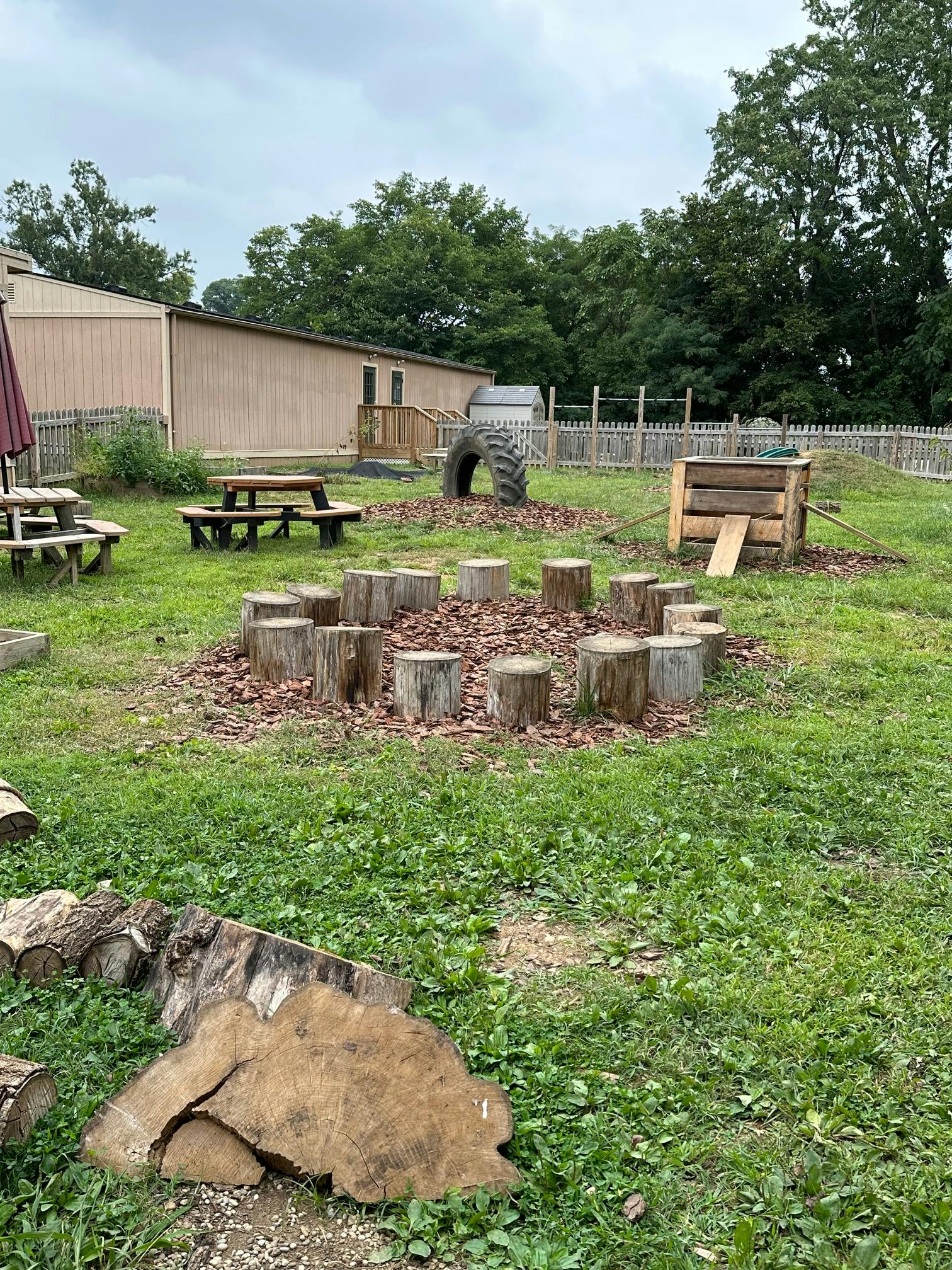 Outdoor play area with tree stumps, a tire, and wooden structures