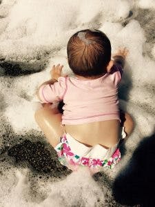Child in a pink shirt and swim diaper sitting in white foam