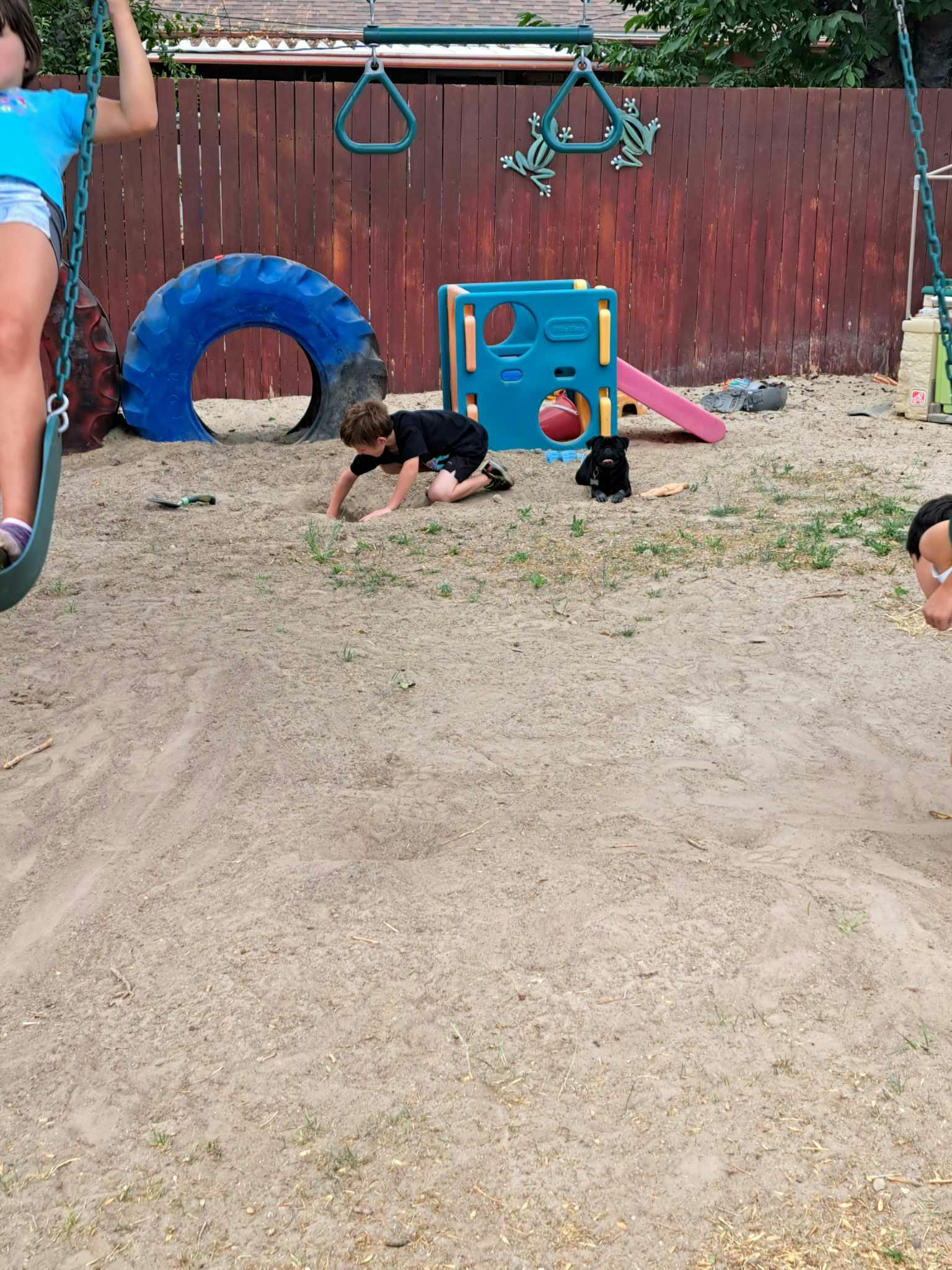 Child on hands and knees in dirt next to playground equipment