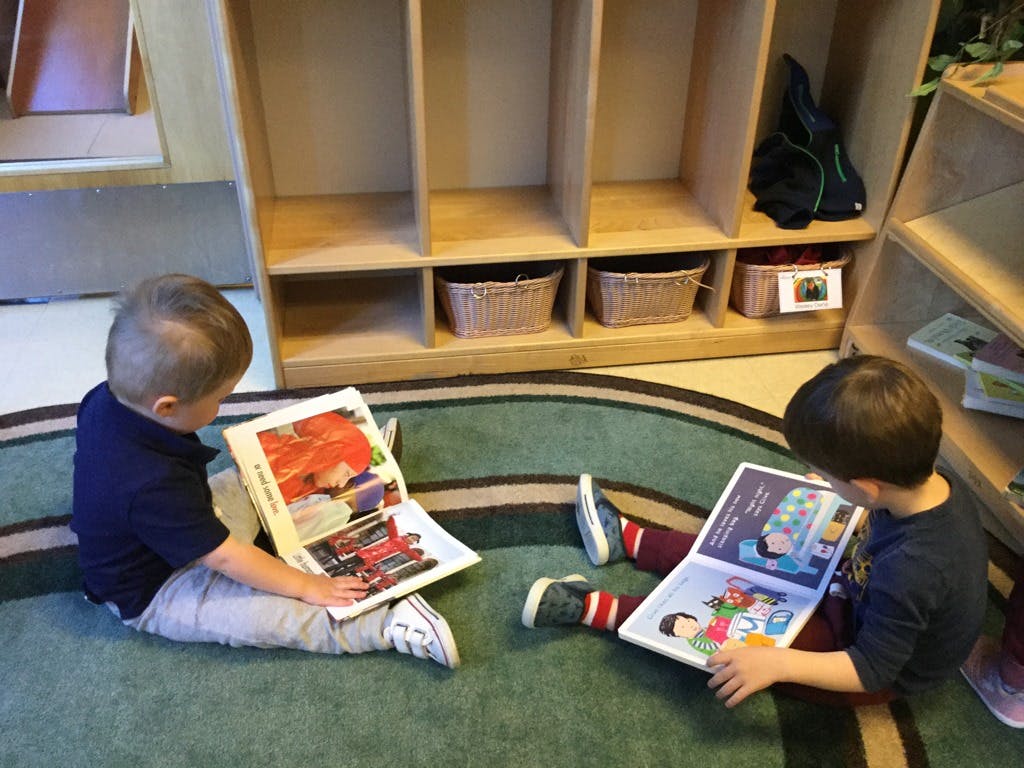 Two children sitting on a rug reading books