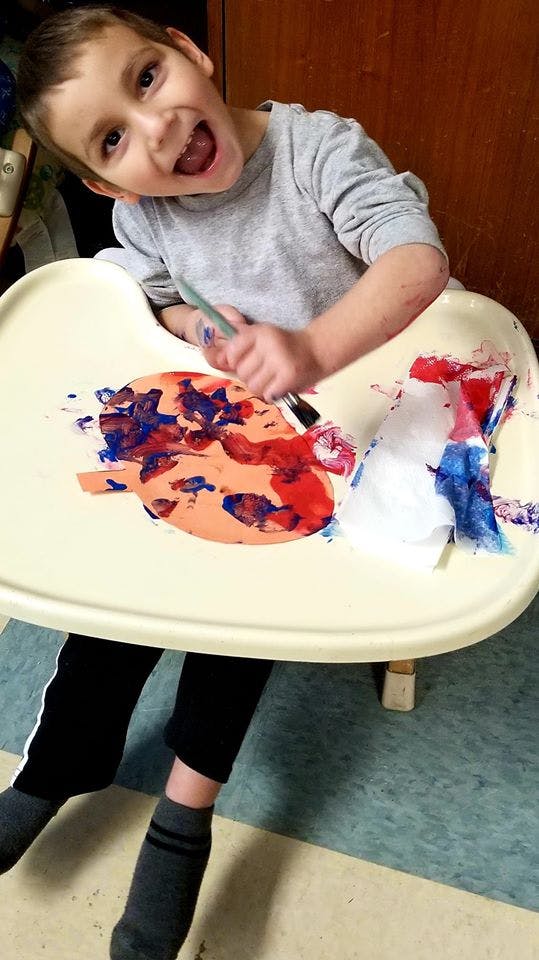 Child painting with red and blue paint on a paper plate in a high chair