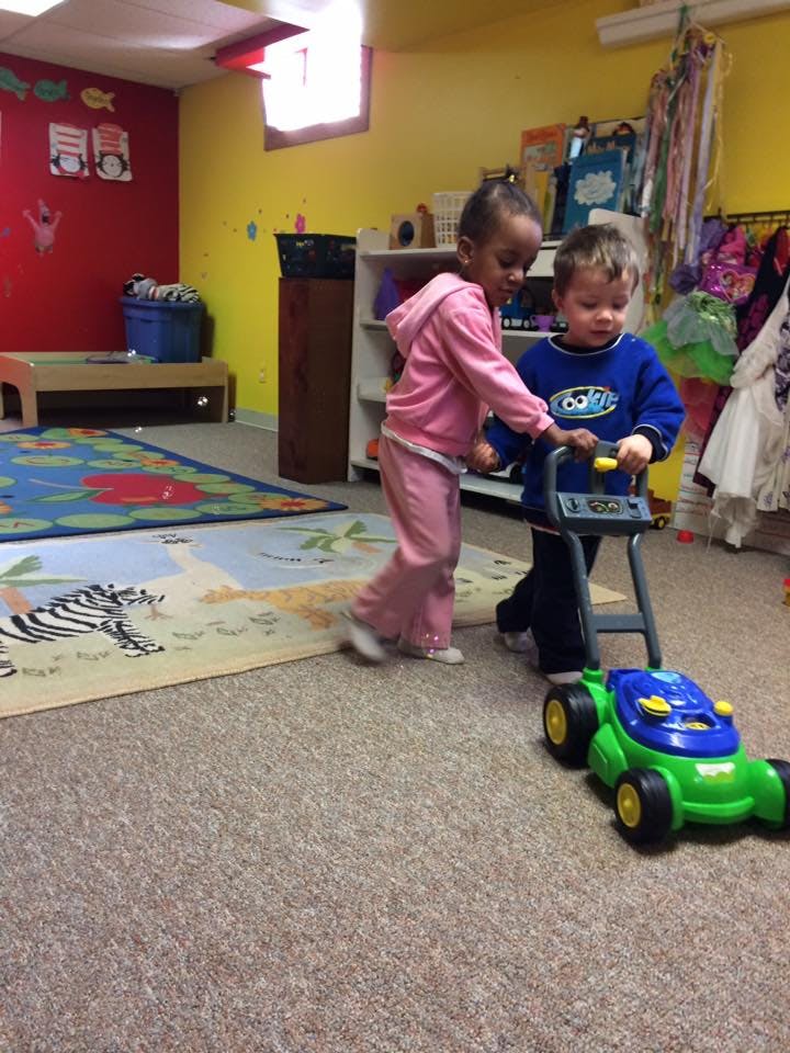 Two children playing with a toy lawnmower in a classroom