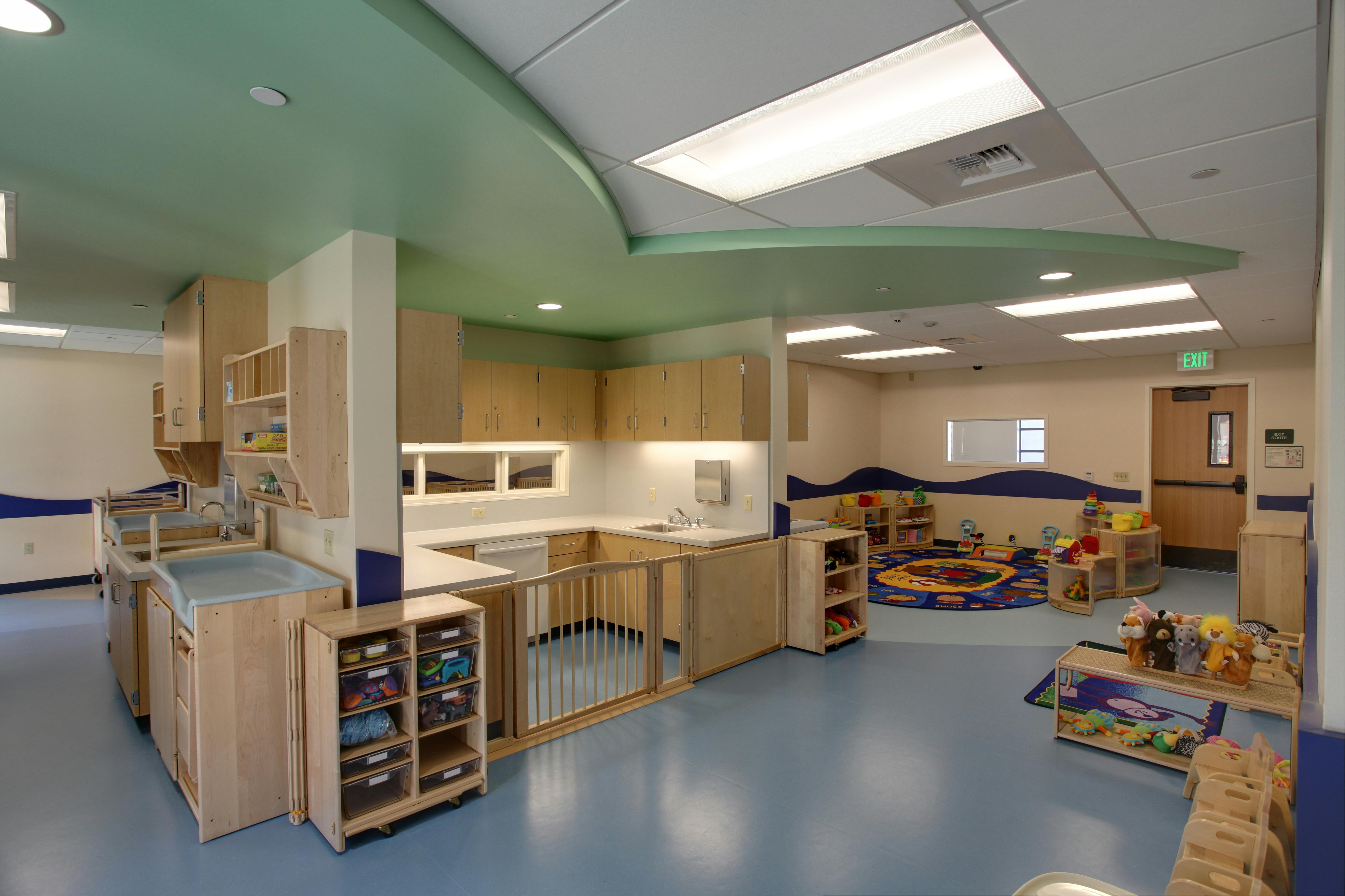 Childcare classroom with changing stations, sinks, play area with rug, and toys