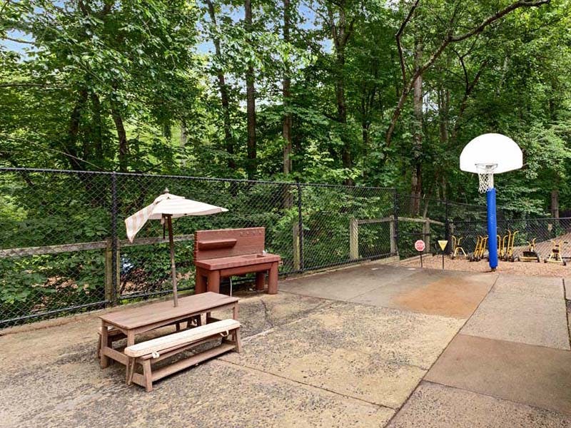 Playground with a picnic table, an umbrella, a basketball hoop, and small tricycles