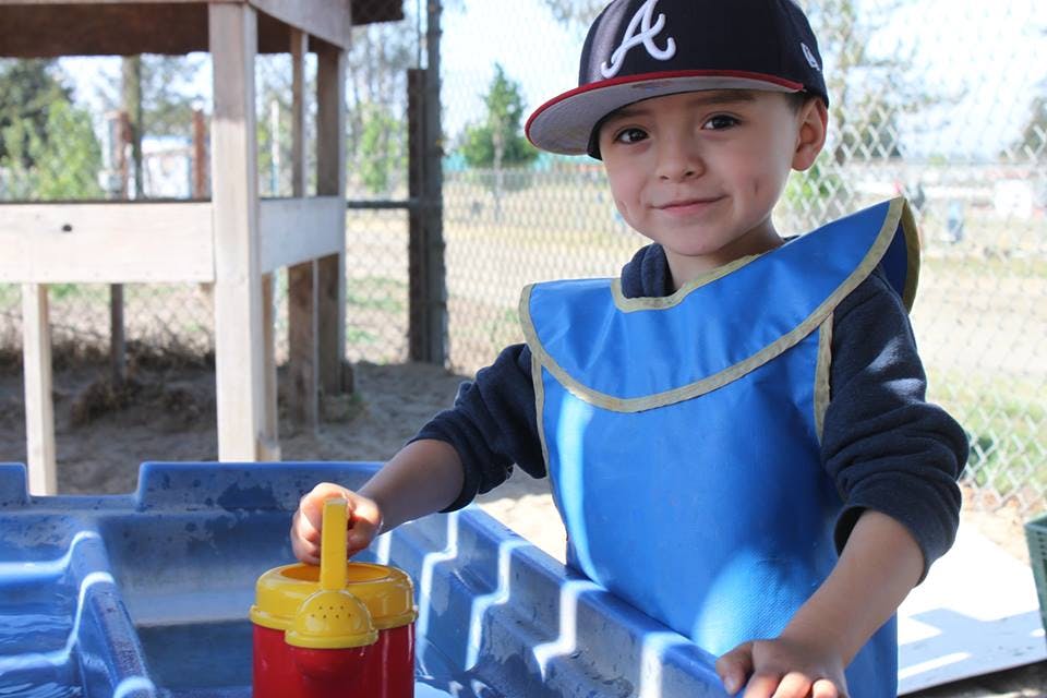 Child in a baseball cap and blue smock playing with a toy