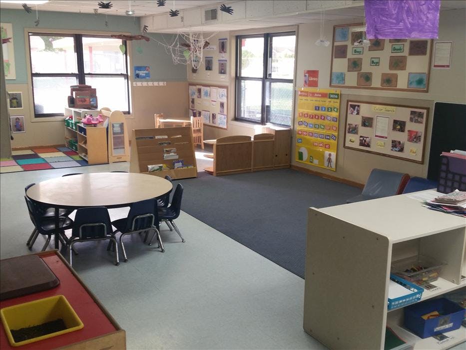 A classroom with small tables and chairs, toys, and learning posters on the wall