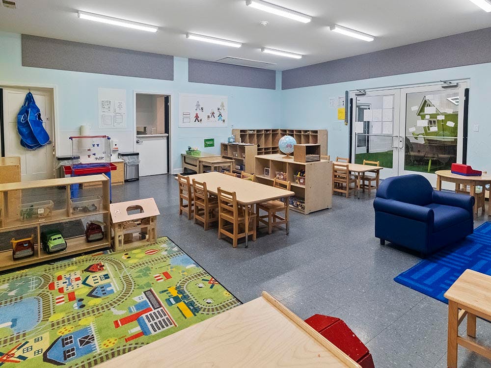 Classroom with tables and chairs, play rug, and blue armchair