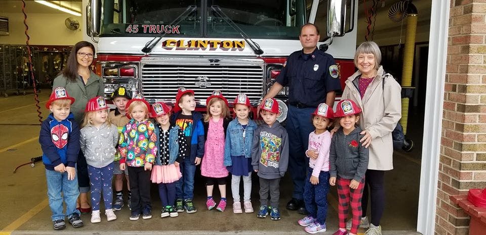 Adults and children in firefighter hats standing in front of a fire truck