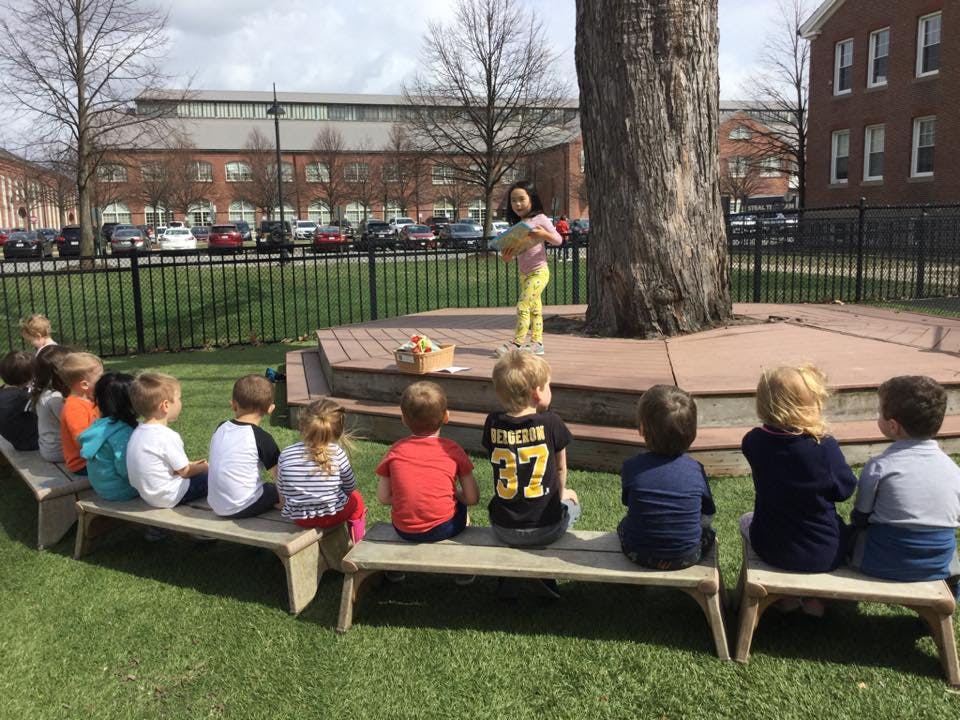 Children sitting on benches watching a person standing on a stage