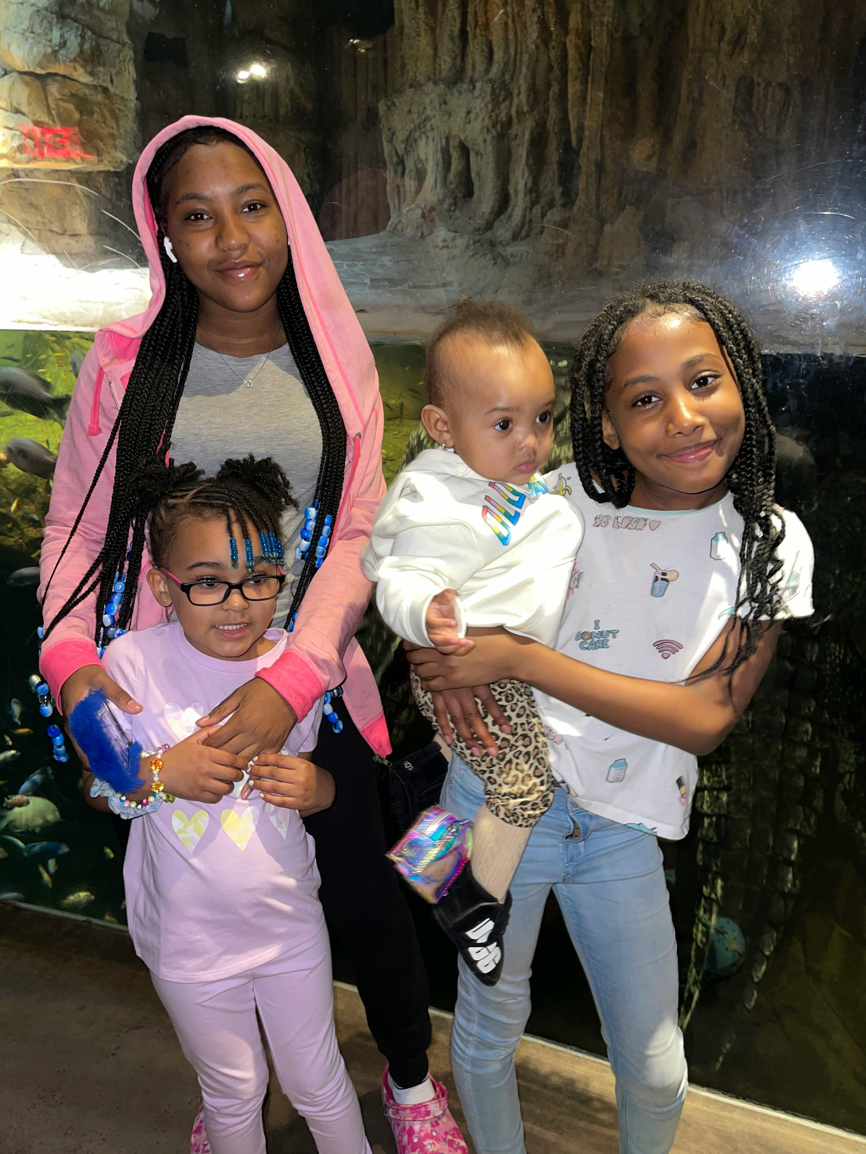 Person in pink hoodie with two children, one child holding a baby