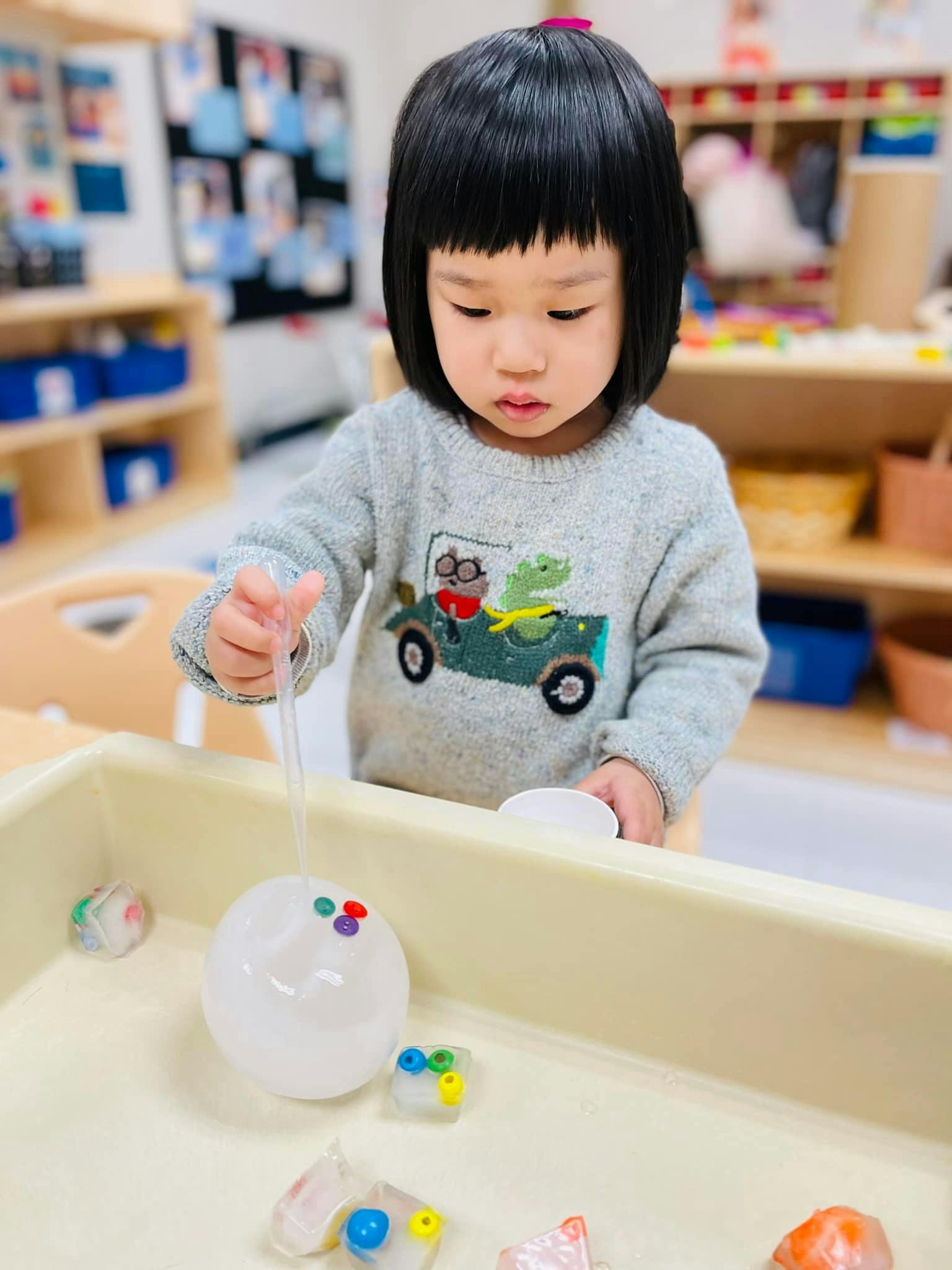 Child playing with a clear ball and ice cubes in a sensory bin