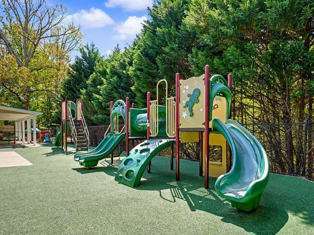 A playground with green slides on artificial turf, surrounded by trees