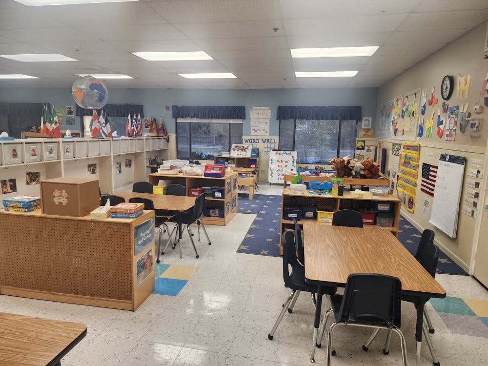An empty classroom with small tables and chairs, shelves, and learning decorations