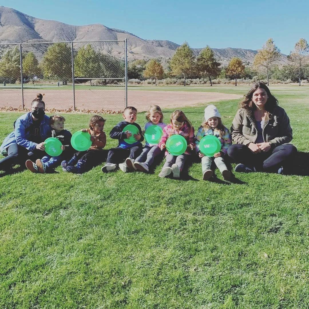 People and children sitting on grass holding green frisbees