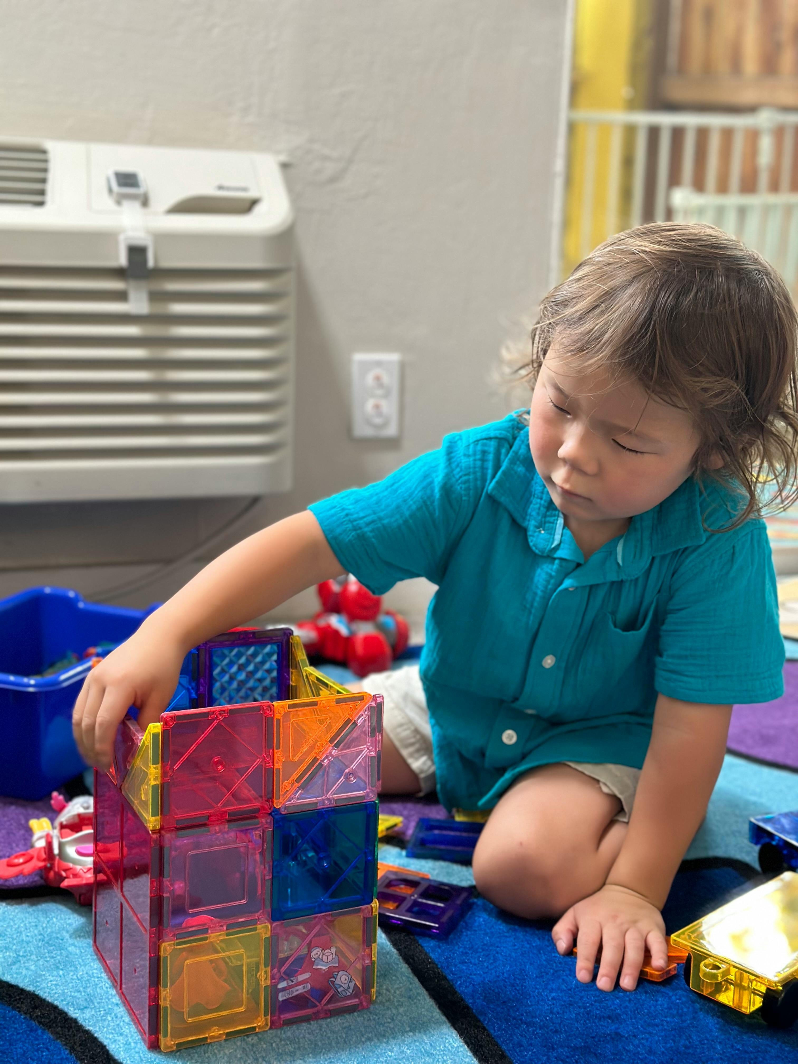 Child playing with colorful magnetic building blocks on a rug