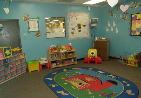 A classroom with blue walls, a colorful rug, and shelves with toys