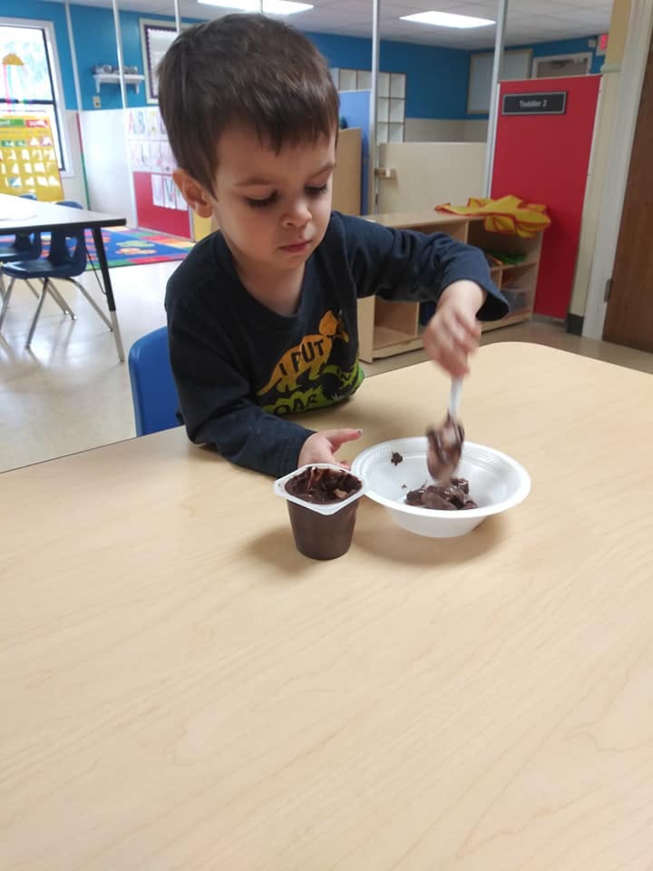Child at a table spooning chocolate pudding from a cup into a bowl