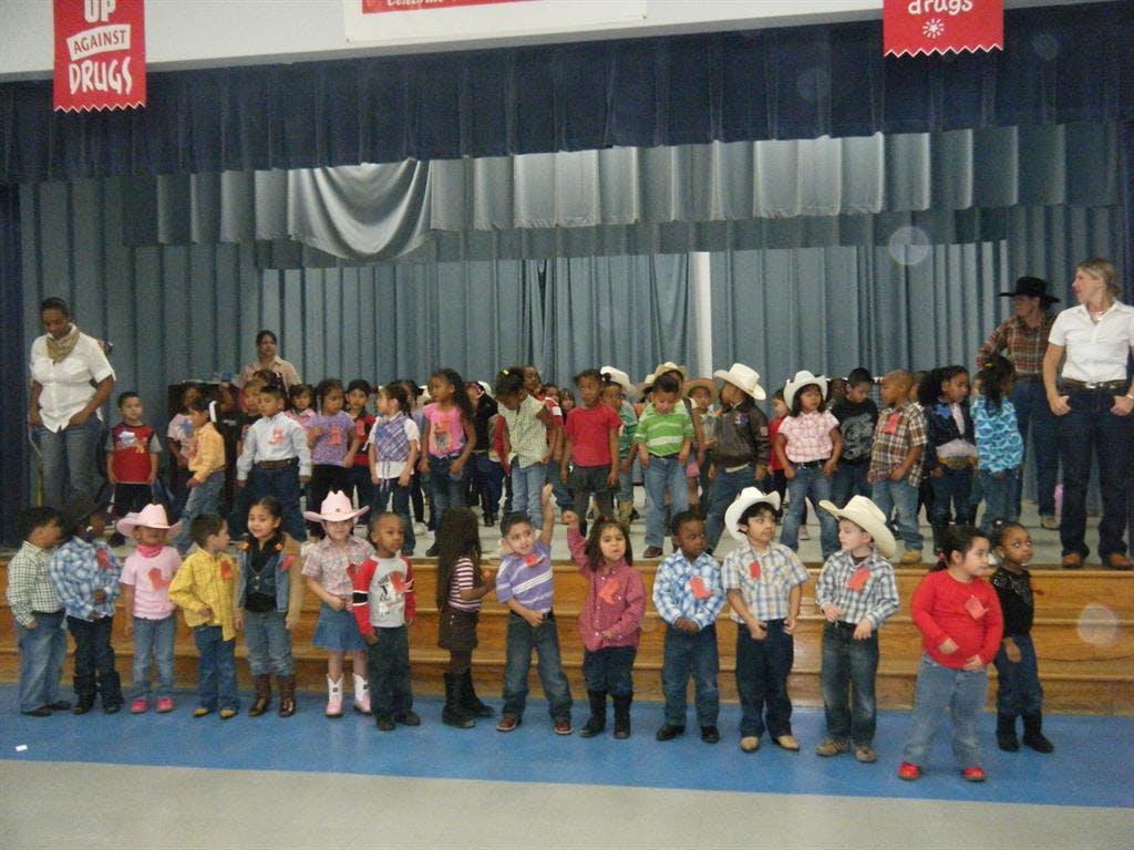 Many children and a few adults on a stage, some children wearing cowboy hats