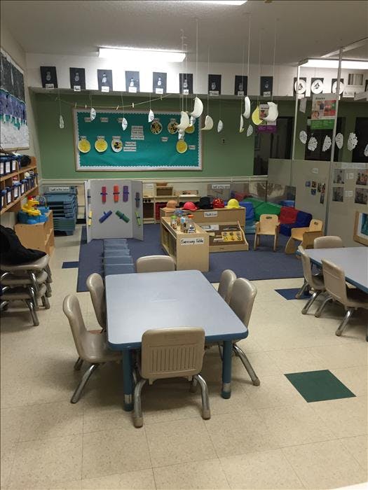An empty early childhood classroom with small tables, chairs, and play areas