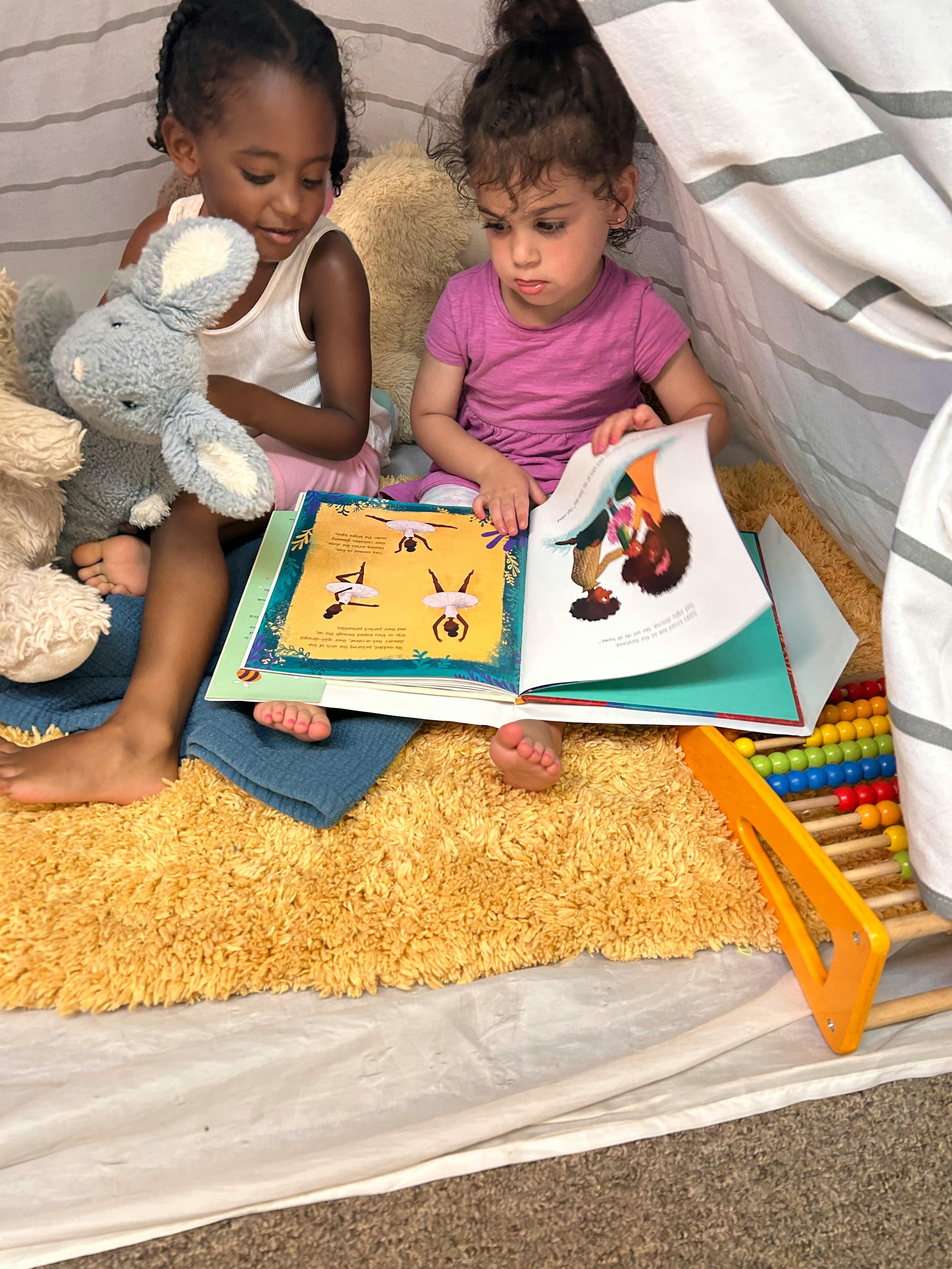 Two children sitting on a rug reading a book together