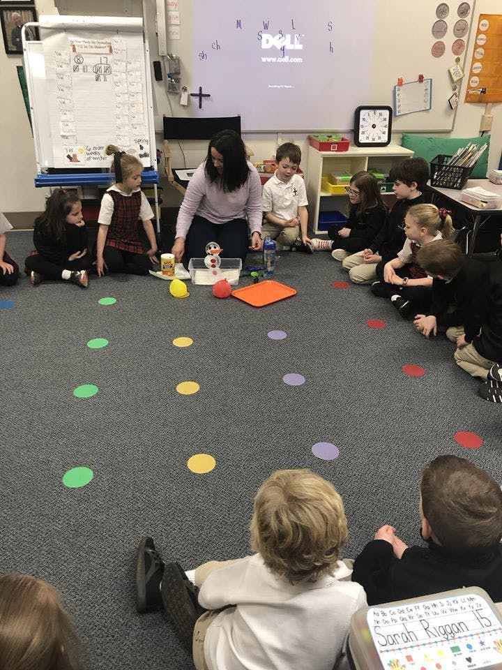 Person kneeling with children sitting in a circle on a classroom floor