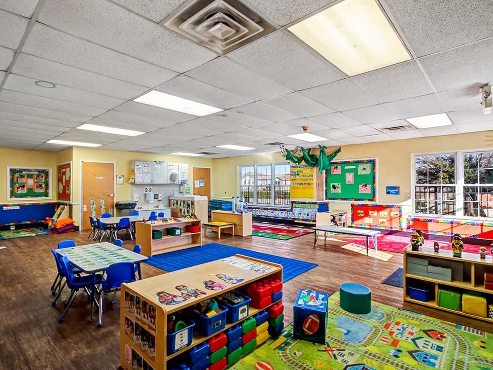 Empty classroom with small tables and chairs, toys, and colorful rugs