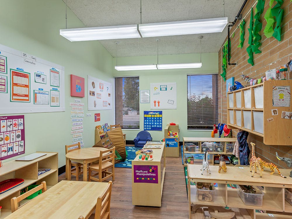 An empty early childhood classroom with small tables, chairs, and learning stations