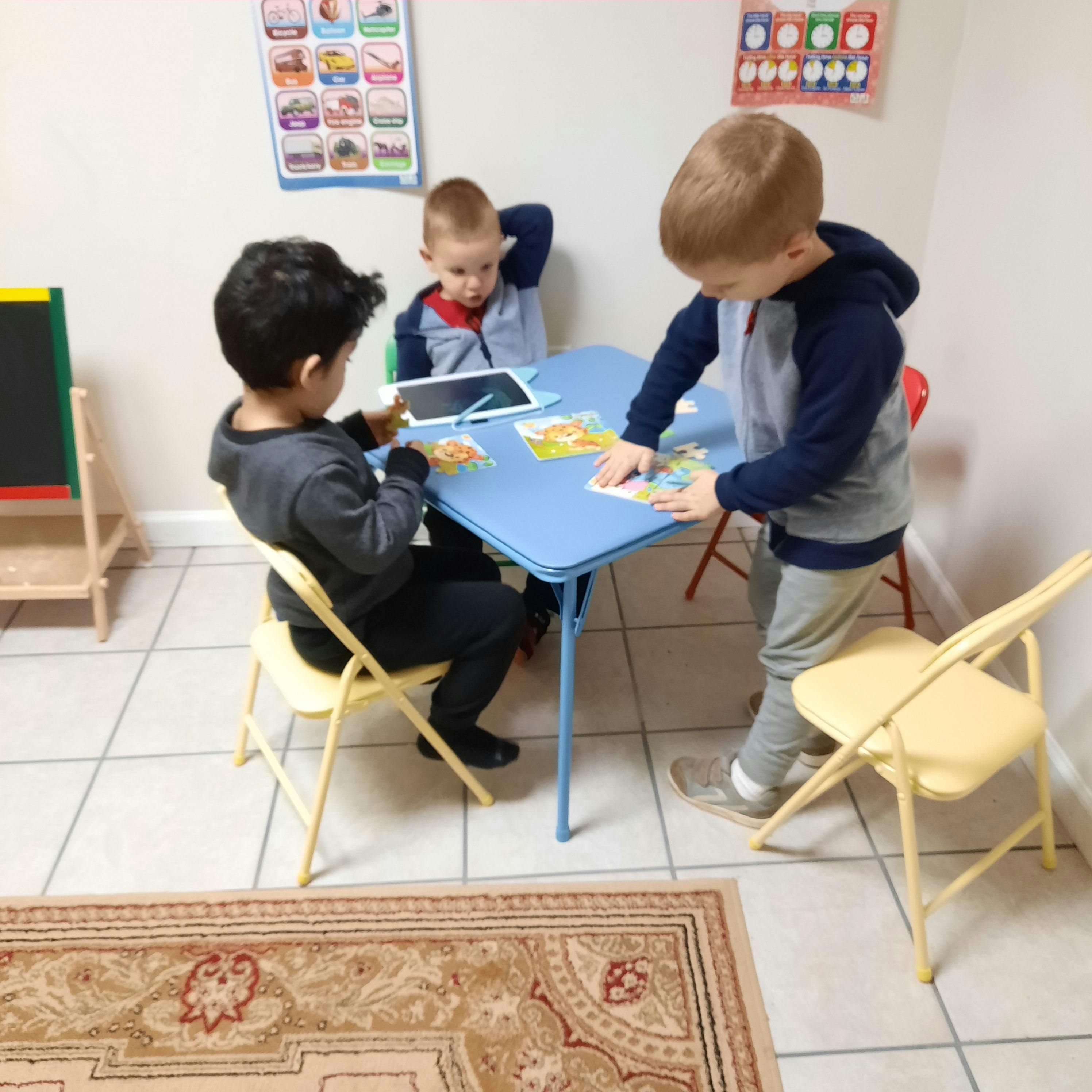 Three children playing at a small table, one using a tablet