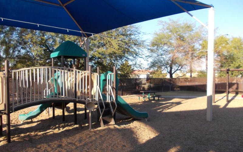 Playground with climbing structure, slide, and picnic table under a blue shade canopy
