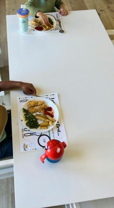 Two children eating meals on placemats at a white table