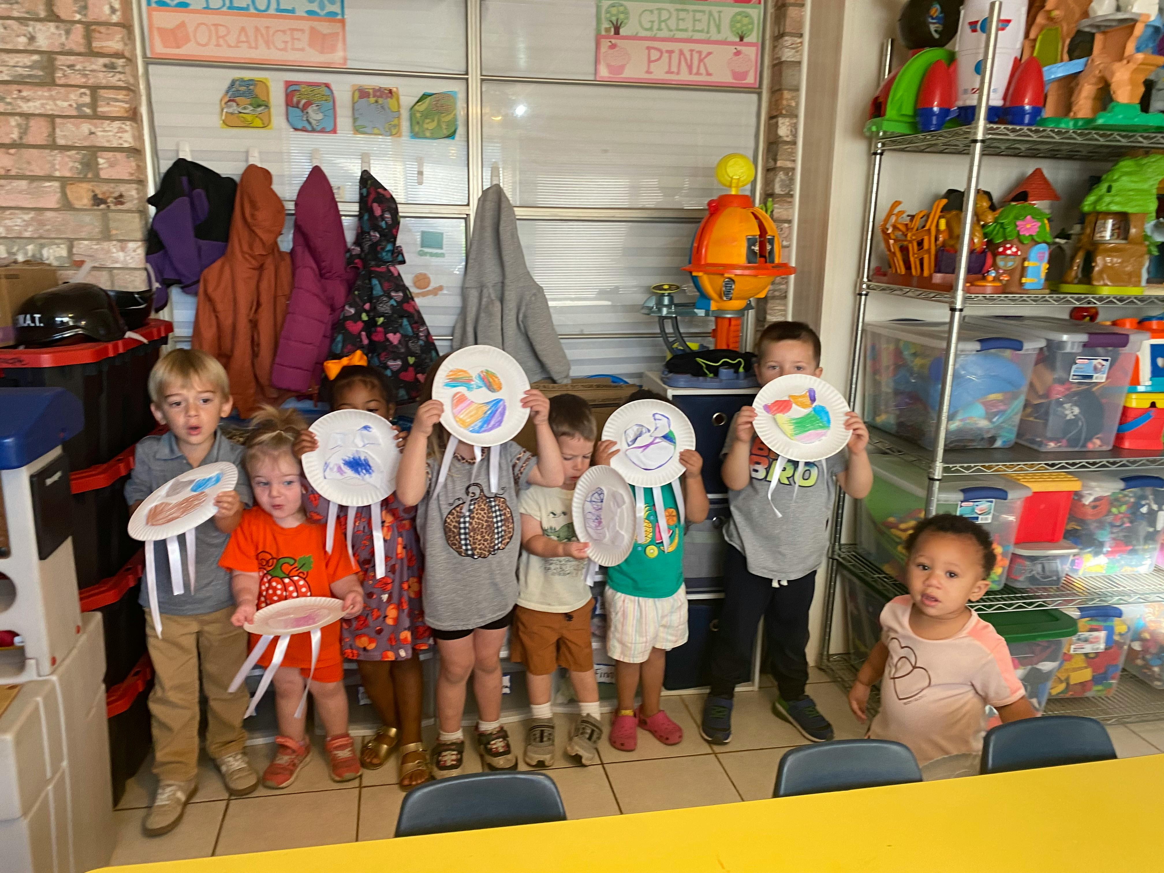 Children holding up paper plate crafts in a classroom