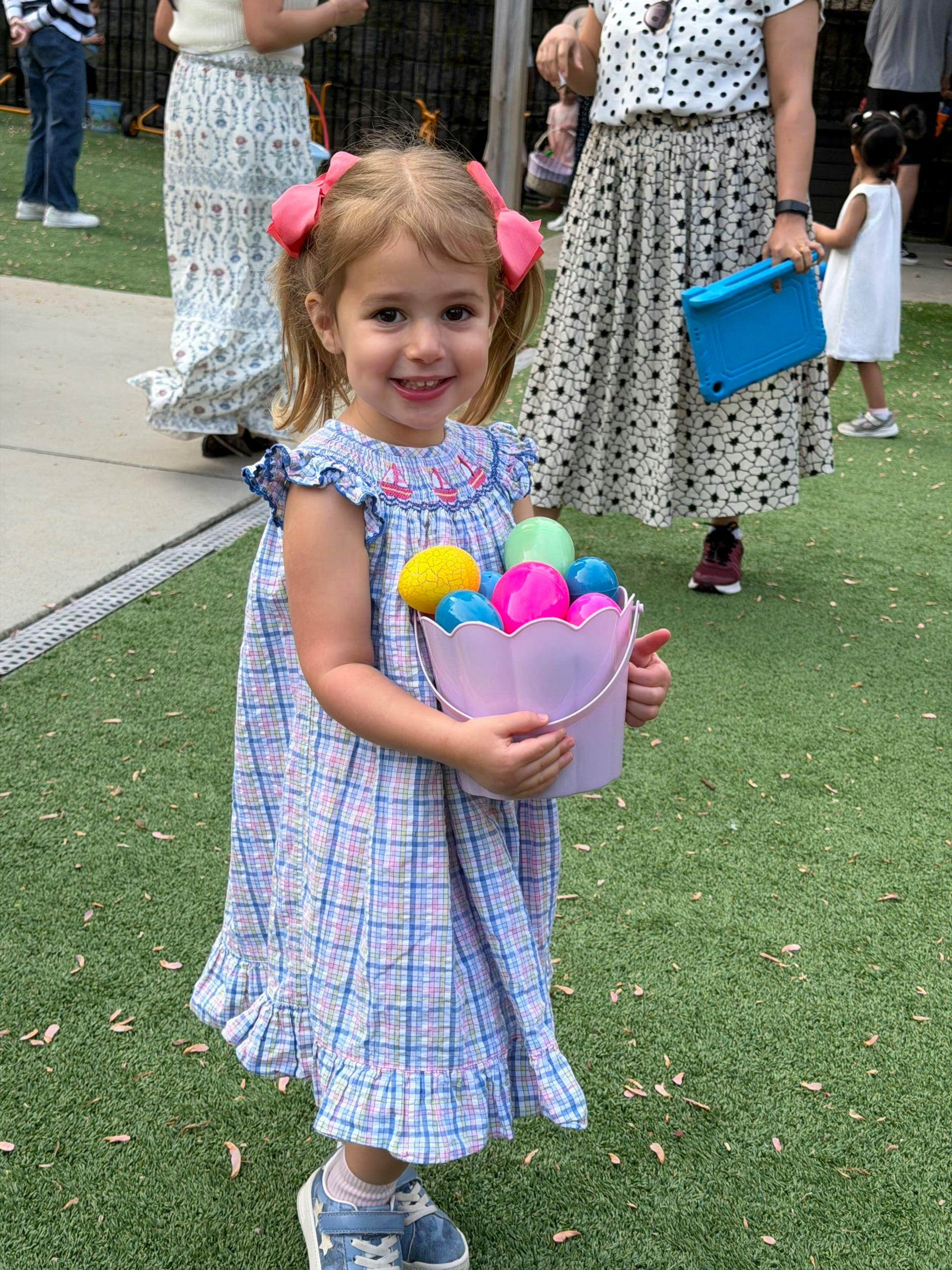 Child holding a bucket filled with plastic eggs on a lawn