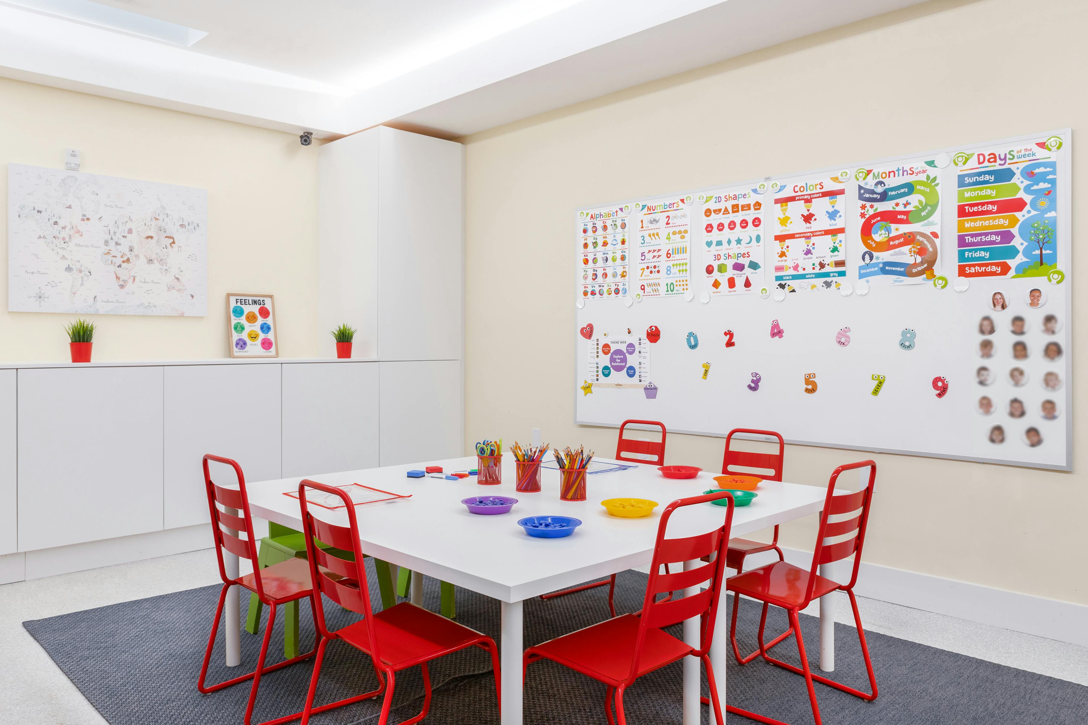 Classroom with a table and red chairs, educational charts on the wall