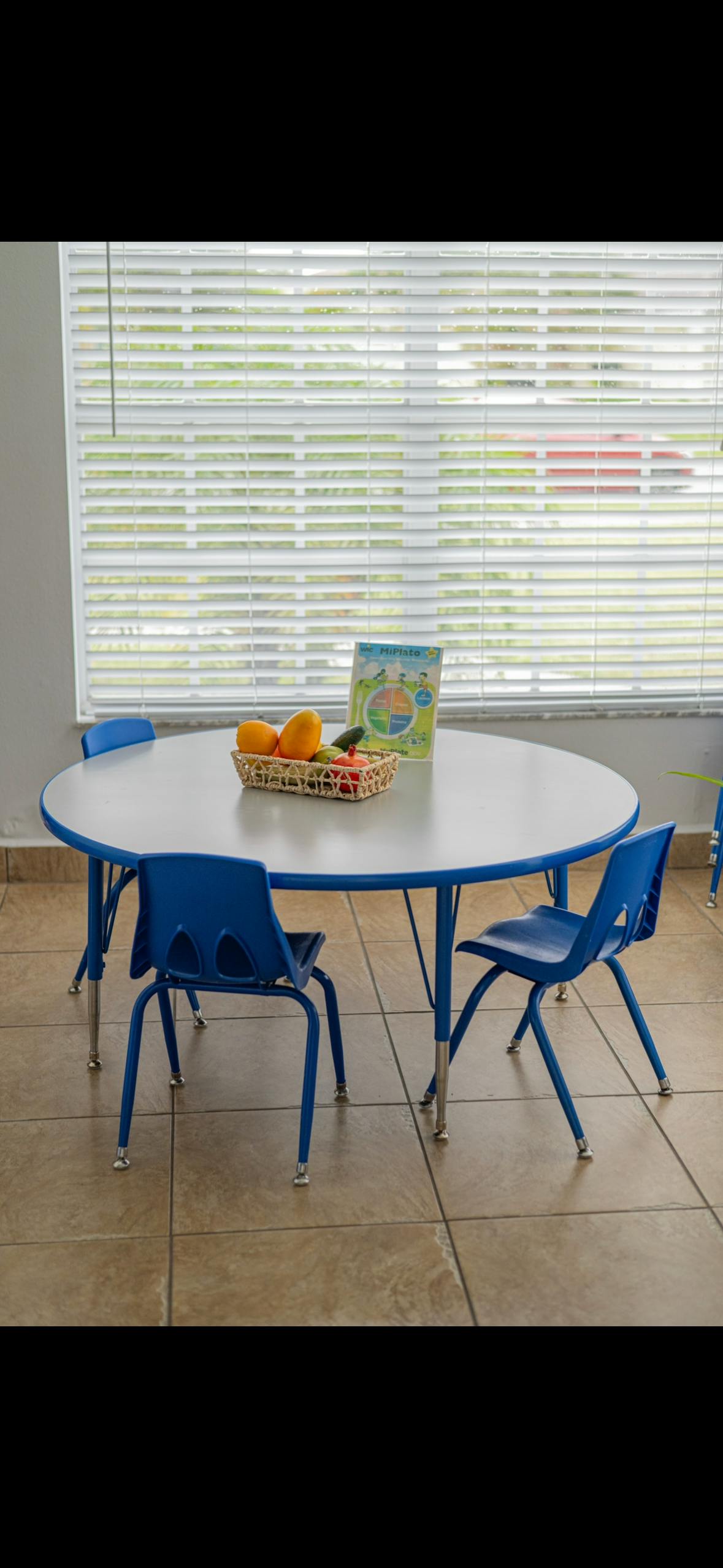 Round table with blue chairs, a basket of fruit, and a book in a classroom