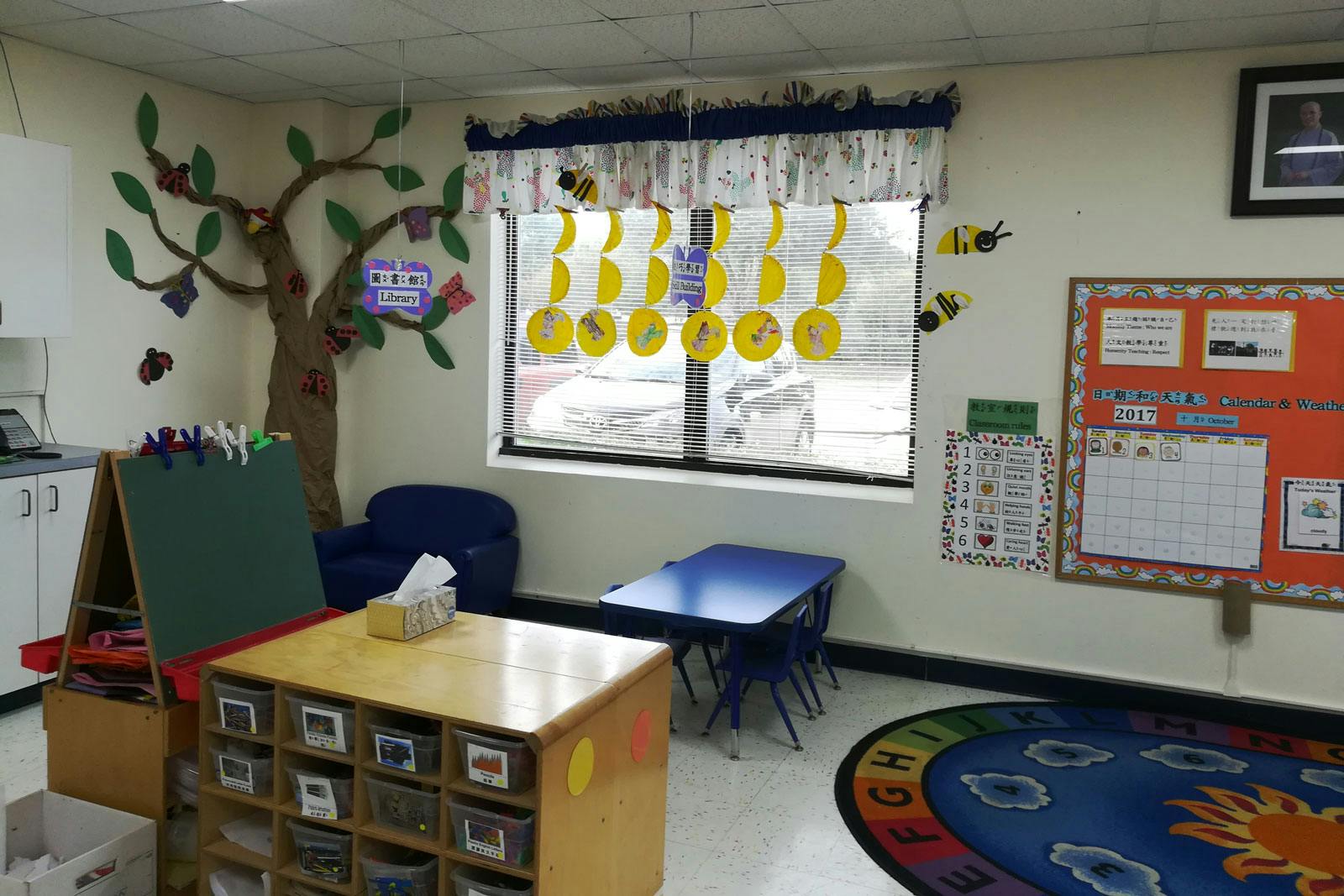 Classroom with small tables, chairs, and a tree mural on the wall