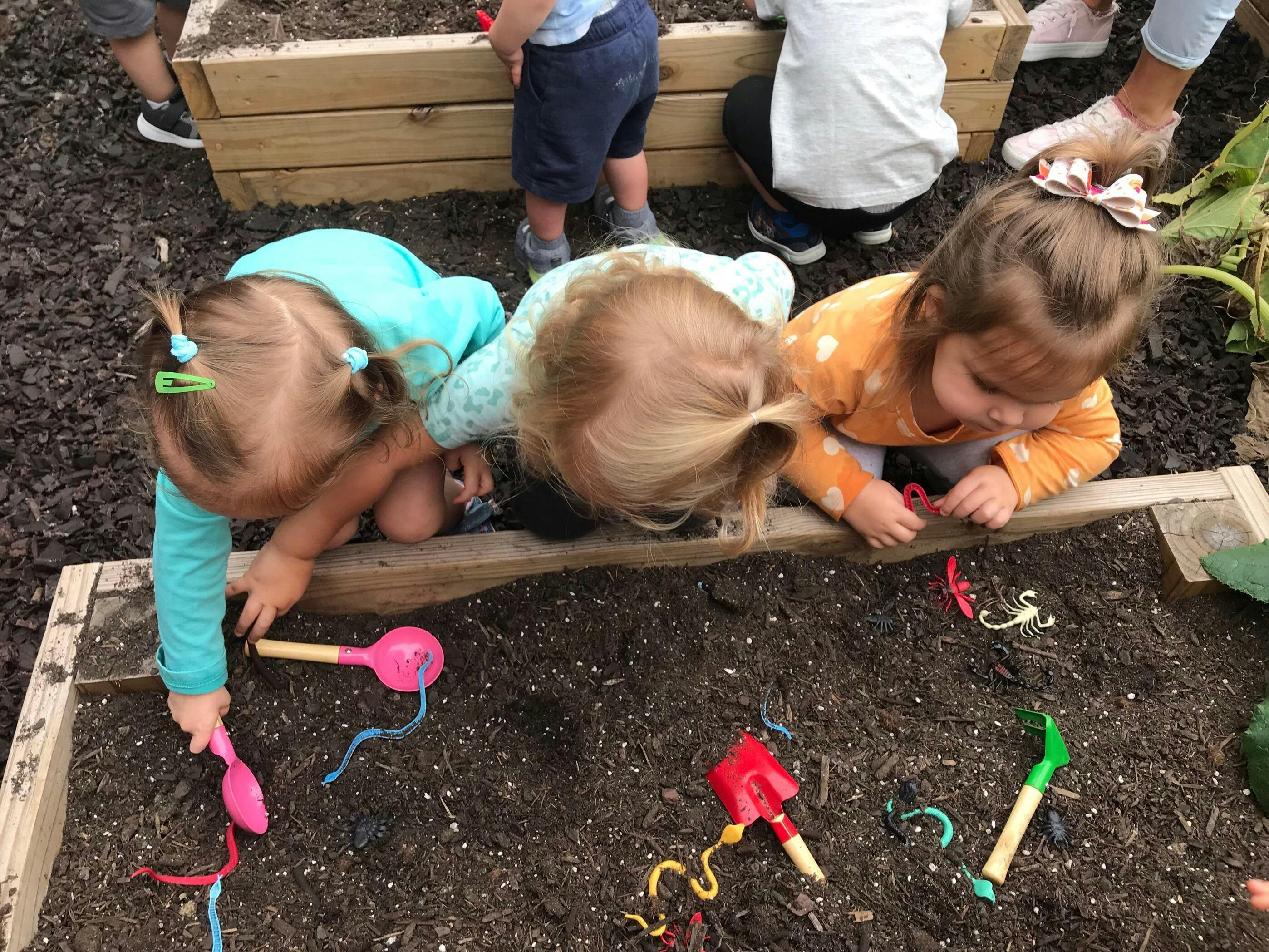 Three children playing in a garden bed with toy shovels