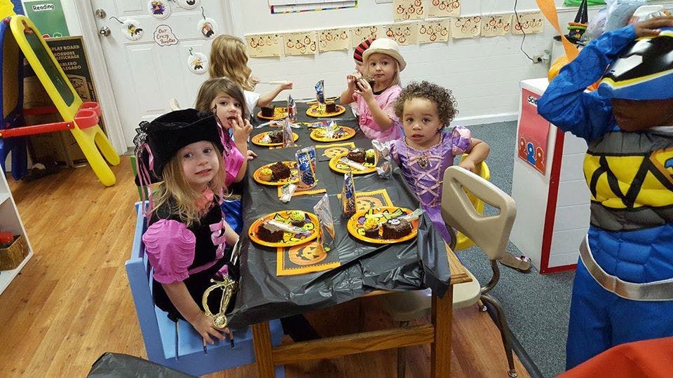 Children in costumes sitting at a table with plates of food