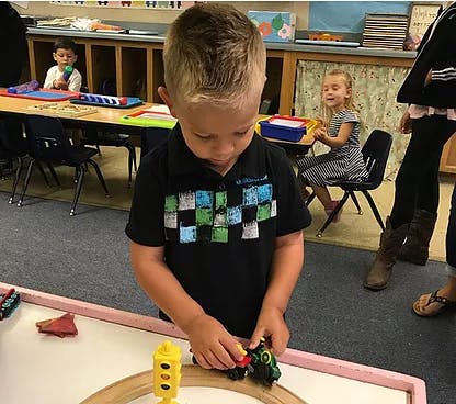 Child playing with a toy train on a track in a classroom