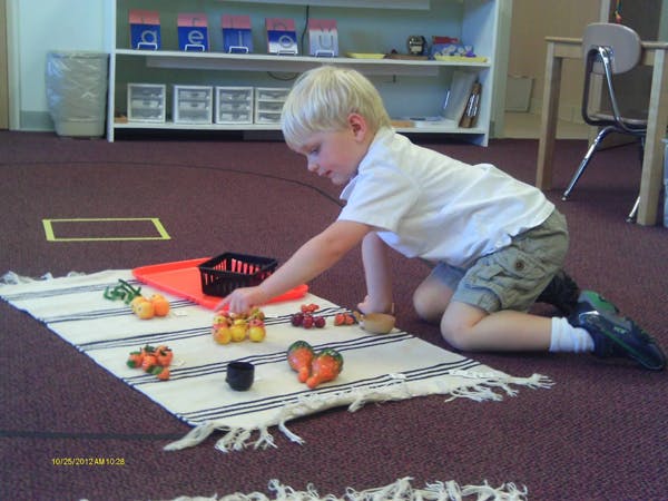 Child kneeling on a rug playing with toy food