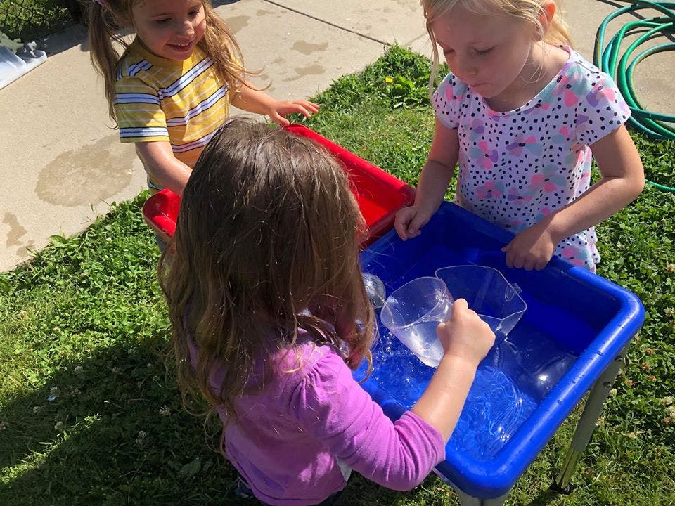 Three children playing with water in a blue bin outdoors