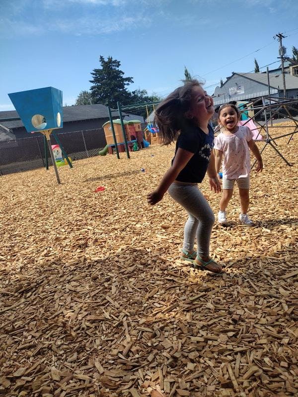 Two children playing on a wood chip playground